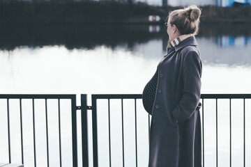 side view of heavily pregnant blonde woman looking at river