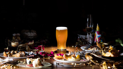 Early morning after the party. Glass of light, cold lager, beer on the table with confetti and serpentine, leftovers, flower petals