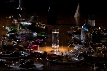 Early morning after the party. Glass of pure, cold water on the table with confetti and serpentine, leftovers, flower petals