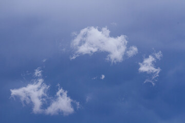 Natural backgrounds. Closeup view of three fluffy white clouds in a stormy blue sky at nightfall. 