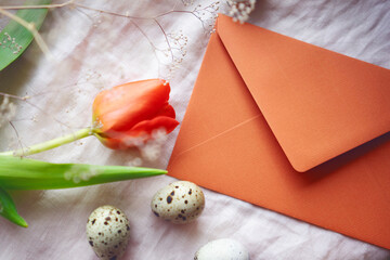 Easter still life with a paper envelope, quail eggs and tulips on a light fabric