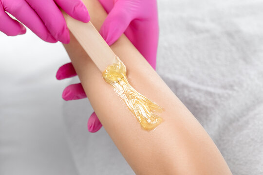 A beautician makes a sugar paste depilation of a woman's arms in a beauty salon.
