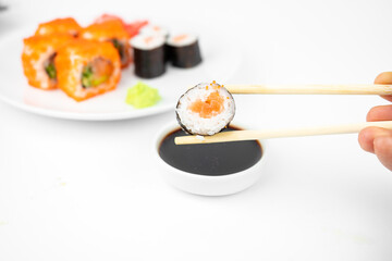 take a california maki rolls with bamboo chopsticks and put in into  soy sauce. pink ginger, wasabi. asian food, japanese cuisine background