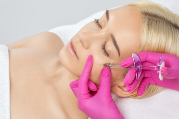 Cosmetologist makes rejuvenating anti wrinkle injections on the face of a beautiful woman. Female...