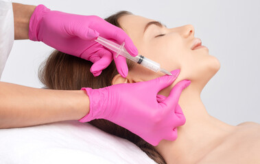 Cosmetologist makes lipolytic injections to burn fat on the chin, cheeks and neck of a woman against double chin. Female aesthetic cosmetology in a beauty salon.Cosmetology concept.