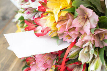 bouquet from multi-colored flowers with empty card or note on the wooden background. multicolored alstroemerias, pink, yellow, purple, white and red alstroemerias