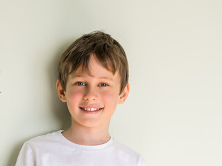 Portrait of smiling 8 year old boy wearing white t-shirt against gray wall with copy space