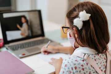 Young elementary school girl with face protective mask watching online education class. Coronavirus or Covid-19 lockdown education concept.