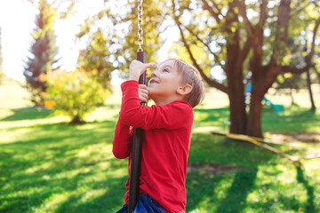 Fototapeta premium Kid swinging on a playground swing in the backyard. Happy healthy childhood.