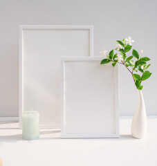 Mock up poster white frame and beautiful Gardenia tropical floral in modern white vase decor with green candle on beige table and cement wall background with long shadow