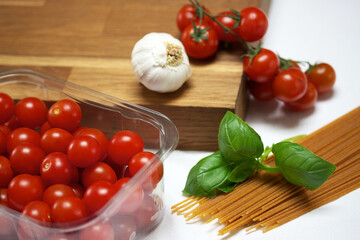 Arrangement of cherry tomatoes with, basil, garlic and  spaghetti on a white background and wooden board