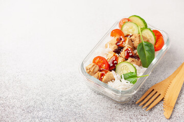 Chicken fillet with rice and vegetables in a glass container on the table. School, sports or business food concept