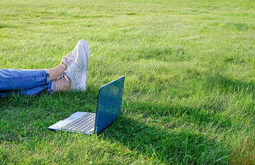 Laptop and legs on green grass. Freelance concept, work or study outdoors. Copy space - Powered by Adobe