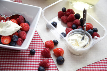 Mixed fruit and cream, with blueberries, strawberries and raspberries set up on a red and white checkered cloth. with summery light 