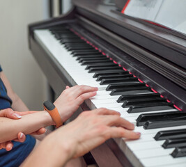 Obraz premium Piano private lesson. Young woman teaches a kid to play the piano. Playing together. Master teaches a boy to play piano. Concept of the music study and arts. Close-up. No faces.