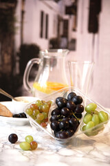 Assorted grapes in container with a  plate of pitta  bread and humus and a jug of water and fruit. with a Mediterranean  background