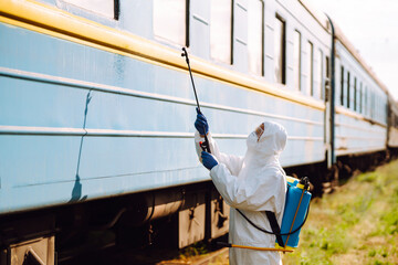 A man in a protective suit disinfects a train. Young man spraying disinfectant on public transportation. Covid-2019. Prevention of spreading  global virus.