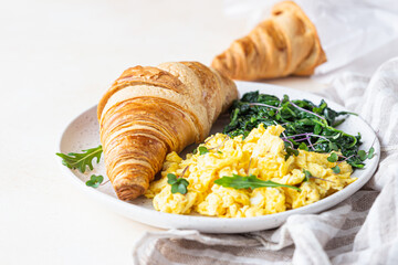 Croissant served with scrambled eggs and spinach on plate, light concrete background. Breakfast.