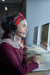 Young operator in headphones talking to customer and working on computer in call center
