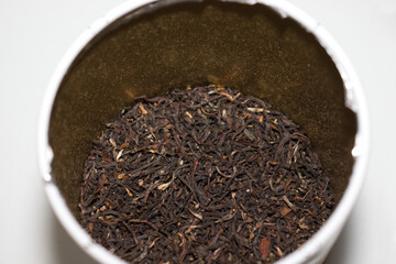 Closeup detail of dry tea leaves in an open tin box on a white background 