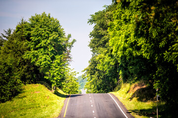 Rural countryside hilly road highway with rolling hills in Virginia with summer trees green canopy, blue sky