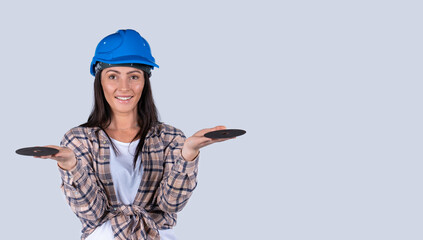 Banner,long format. A handyman woman in a blue helmet looks into the camera with a smile and holds abrasive discs with both hands. White background. Place for advertising.