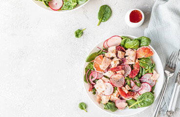 Fresh salad with salmon, spinach, radish and red oranges served with orange sauce, light concrete background. Top view.