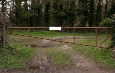 A  closed rusty metal gate with a white sign across a farmers field