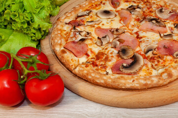 Pizza with ham, mushrooms and cheese on a board with tomatoes and green salad