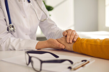 Closeup shot of female doctor hold male patient hand over desk. Specialist give medical or psychology help, trust, support, encourage and reassure during meeting. Medicine and health care