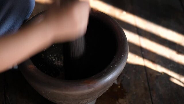 4K Close up hands of asian child boy playing with mortar and pestle in rural kitchen. Kid helping cook food. Concept of family activity.