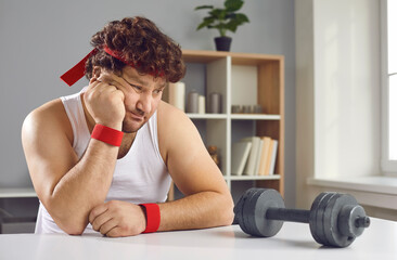 Funny sceptic lazy curly man looking thoughtfully at small barbell unsure whether he needs sports exercise. Sad fat man afraid of failure has no motivation to start training with dumbbells at home - obrazy, fototapety, plakaty