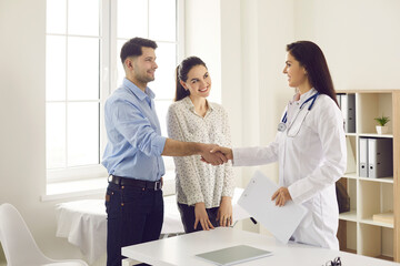 Fototapeta premium Planning future baby. Married couple shakes hands with a female gynecologist while getting acquainted during a clinic visit. Happy future parents at the consultation of an experienced doctor.
