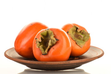 Three ripe organic persimmons on a clay plate, close-up, isolated on white.