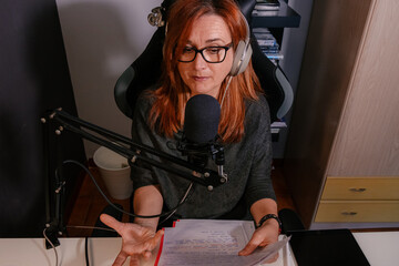 Mujer caucásica de mediana edad grabando un podcast desde casa en el escritorio junto a un...