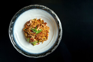 Sweet and sour noodles with pork, peanuts, vegetables and onions, served in a white bowl. Wok noodles. Isolated on a black background. Street thai food