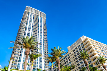 Oceanfront apartment skyscrapers buildings along coast in Miami Beach, Florida with green palm trees on sunny summer day - obrazy, fototapety, plakaty