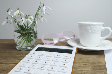 Obraz na płótnie Canvas electronic white calculator, a cup of coffee, cappuccino, women's glasses, records of calculations, concept of recording debit and credit, the workplace of accountant, home economics, coffeetime