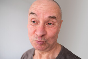 face of a European old man close up, wrinkles on the aging skin, bares teeth, makes grimaces, the concept of mental health, cosmetology, age-related changes
