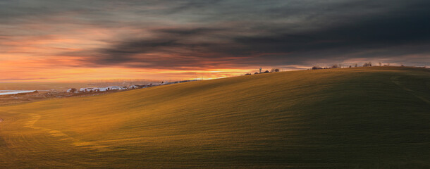 Large farm field on the hill. Agricultural land at sunset background. Rural field, farm on the edge...