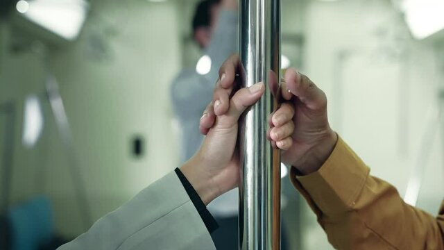 The hand of a man harassing a woman's hand clinging to a rail on a public transportation system at night
