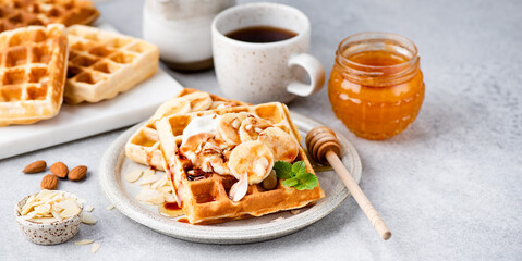 Sweet belgian waffles with banana and caramel sauce on a plate. Breakfast food waffles and coffee