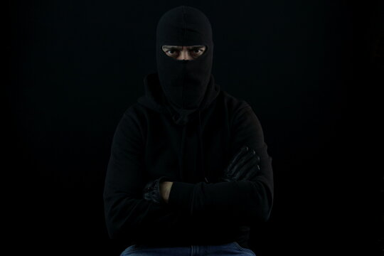Portrait man with balaclava sitting with crossed arms looking at the camera. Crime concept