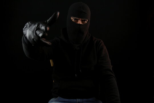 Man with balaclava sitting making the gun gesture with hand and fingers looking at the camera. Crime concept