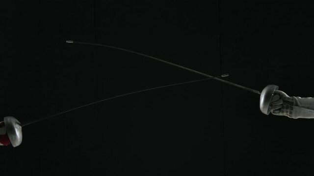 Hands of female fencers with rapiers close up on a black studio background. Women masterfully fight with combat swords, practicing attacks and defense techniques. Slow motion.