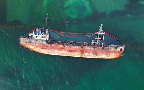 The Old Rusty Ship Was Stranded By A Storm. Oil Spill From A Tanker, Environmental Pollution. Top View Of A Rusty Ship In The Sea.