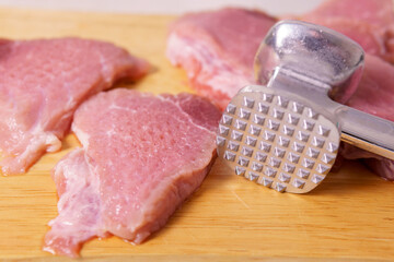 Cooking pork meat chops. Raw slices of pork meat are beaten with a kitchen hammer on a wooden board before cooking. fresh raw meat