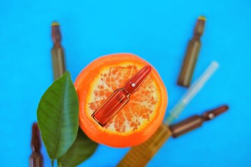 Vitamin C. Serum with Vitamin C. Glass ampoules close-up set and syringe with injection solution on tangerines fruits with bright green leaves on blue background.Beauty and health concept