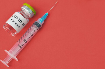 Syringe and Covid-19 bottle vaccination over red background.