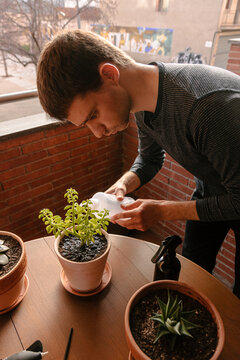 Hombre joven cauc&aacute;sico regando una planta encima de la mesa de la terraza de su casa. Cuidando plantas 